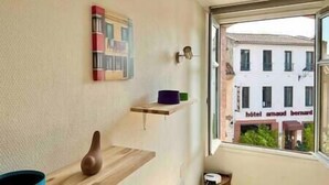 Une pièce avec une fenêtre, une étagère en bois, un tableau accroché au mur et une petite table.