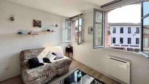 Un salon avec un canapé, une table basse et une grande fenêtre donnant sur un immeuble.