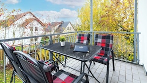 Een balkon met een tafel en stoelen, een laptop en een plant in een pot.