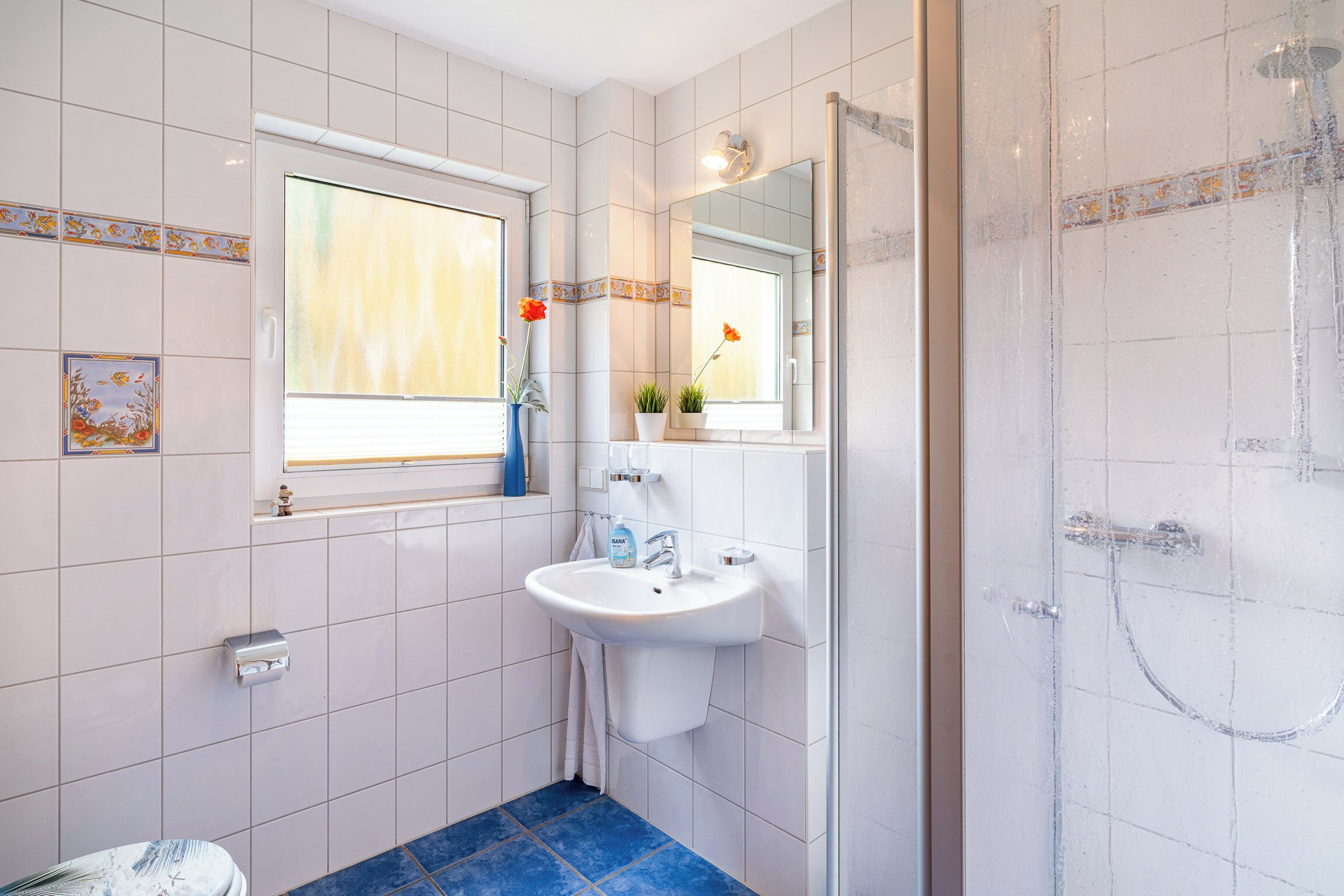 A bathroom with a sink, mirror, window, and shower.