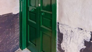 A green door with a red emergency light, a white wall with peeling paint, and a speckled floor. - Casa Pulcinella a Spaccanapoli by Wonderful Italy (Naples)