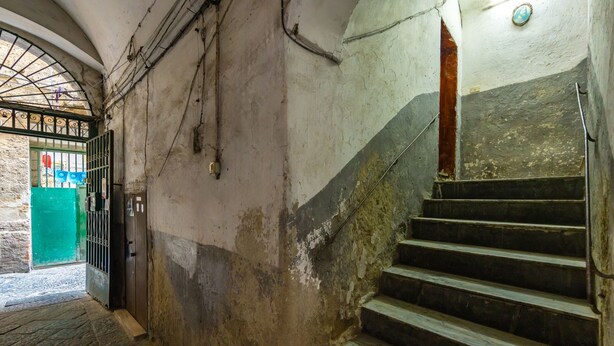 A staircase with a handrail, a green door with a metal gate, and a stone floor. - Casa Pulcinella a Spaccanapoli by Wonderful Italy (Naples)