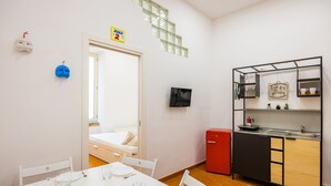 A compact room with a bed, a dining table with chairs, a small kitchenette, and a TV. - Casa Pulcinella a Spaccanapoli by Wonderful Italy (Naples)