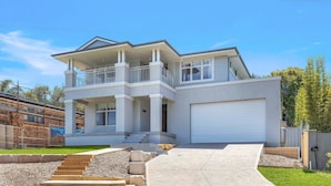 A two-story house with a balcony, a garage, and a driveway leading to the entrance. - Coastal Ambience by HolidayCo. (KILLCARE HEIGHTS)