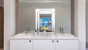 A modern bathroom with a large mirror, two sinks, and a vase with flowers. - Coastal Ambience by HolidayCo. (KILLCARE HEIGHTS)