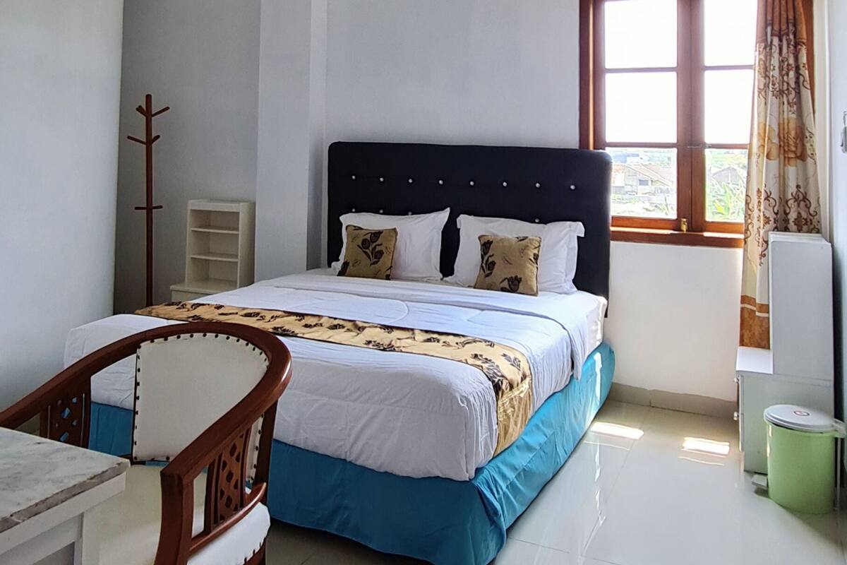 Une chambre à coucher avec un lit, une chaise, un radiateur, une fenêtre avec des rideaux et une poubelle.