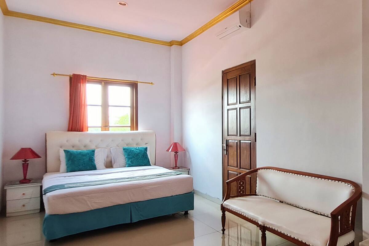 Une chambre à coucher comprenant un lit, une chaise, une table de chevet, une fenêtre avec des rideaux et une porte.