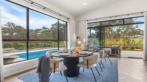 Un comedor con vista a la piscina, amplias ventanas y un espacio de estar exterior informal.