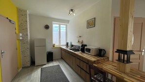 A compact kitchen with a refrigerator, microwave, and coffee maker on the counter, a wooden chair, and a small window with a view. - Cramiland - Appart 01 Ohnenheim (Ohnenheim)