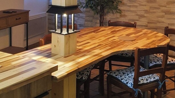 A dining area with a wooden table and chairs, a potted plant, and a wall with a stone-like texture. - Cramiland - Appart 01 Ohnenheim (Ohnenheim)