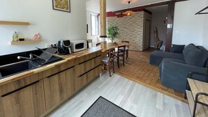 A modern kitchen with a wooden countertop, a microwave, and a coffee maker. There is a dining area with a table and chairs, and a living room with a sofa and a coffee table. - Cramiland - Appart 01 Ohnenheim (Ohnenheim)