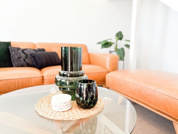 A modern living room with a glass coffee table, a green decorative object, and a white object on a woven placemat.