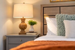 A neatly made bed with a white pillow and a green throw, a bedside lamp, a small potted plant, and a book on a nightstand. - The Sundancer Oasis|Old Town|Pool+Spa|Rooftop Deck (Scottsdale)