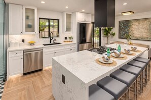 A modern kitchen with white cabinetry, a central island with bar stools, a stainless steel dishwasher, and a large window. - The Sundancer Oasis|Old Town|Pool+Spa|Rooftop Deck (Scottsdale)
