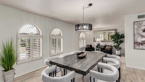 Un coin repas avec une table en bois et six chaises, un lustre et un grand miroir au mur.