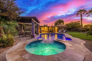 A swimming pool with a stone deck, a covered patio area, and a view of a house with a patio.