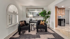 Un salon moderne avec deux fauteuils noirs, une table basse, un grand miroir et une plante en pot.