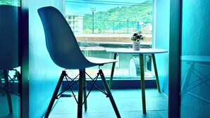 A modern room with a large window, a chair, and a small table with a vase of flowers. - THE NICE  (Patong)