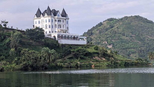 A large, white, castle-like building with multiple towers, situated on a hillside by a body of water. - chateau le marara (Bwishyura)