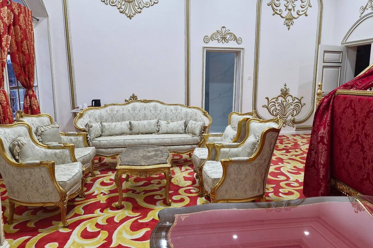 Une chambre luxueuse avec un canapé blanc, des motifs dorés raffinés et un tapis rouge à motifs.