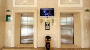 An elevator area with two elevators, a television mounted above, and a small trash bin in the center. - Vienna hotel shenzhen shajing shangnan  (Shenzhen)