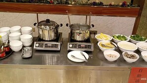 A buffet setup with multiple food stations, including a hot pot, salad, and various condiments. - Vienna hotel shenzhen shajing shangnan  (Shenzhen)