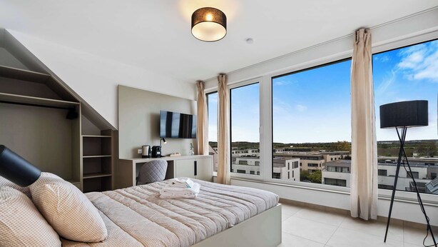 A modern bedroom with a large bed, a TV, and a view of the city.