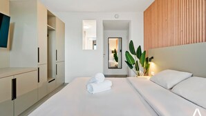 A modern hotel room with a large bed, a wooden headboard, a TV, and a wardrobe.