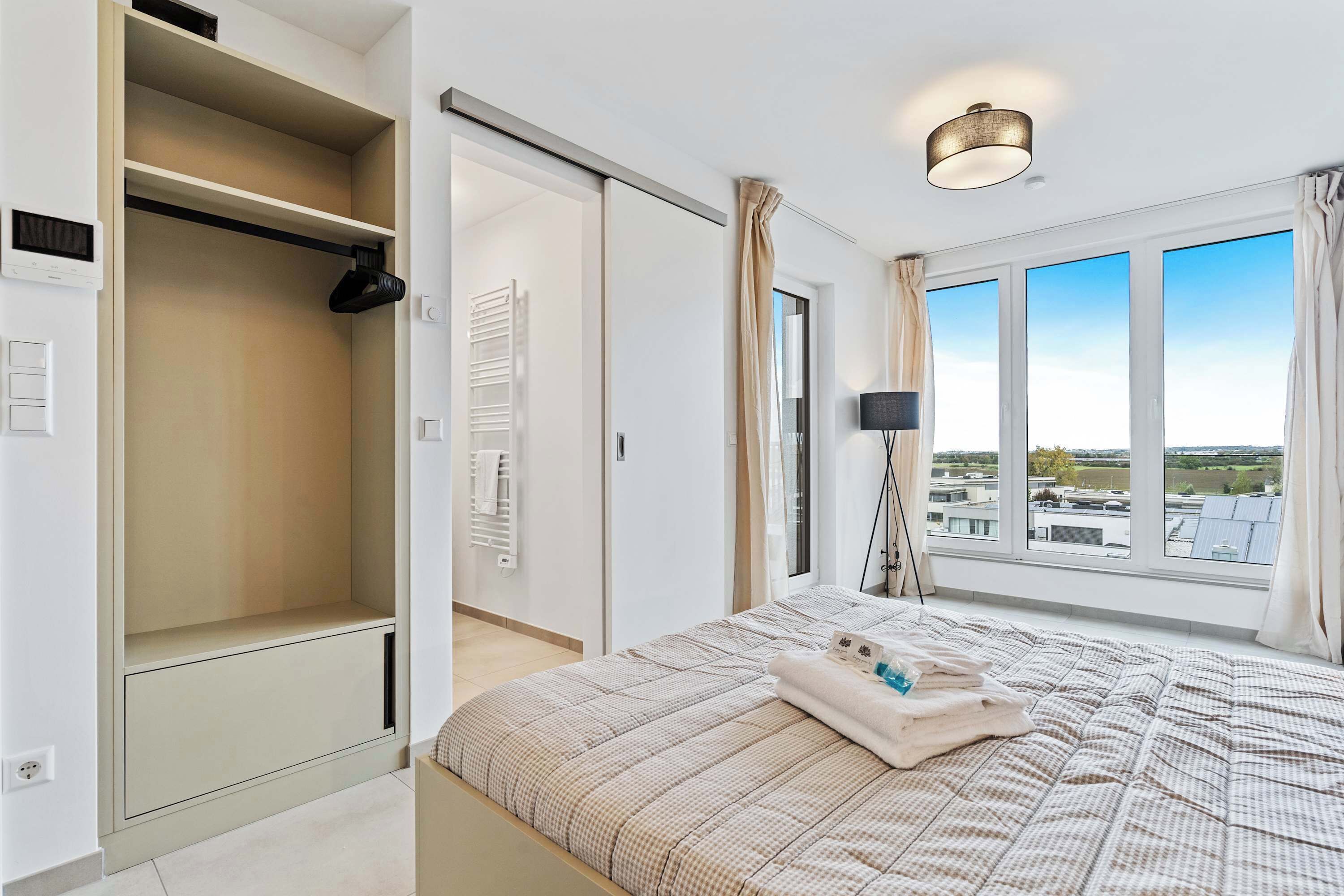 A bedroom with a large bed, a wardrobe, a sliding door, a window with a view, and a ceiling light.