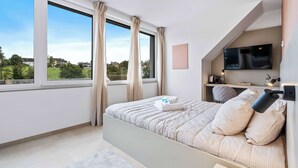 Ein Schlafzimmer mit großem Fenster, einem Bett, einem Fernseher und einem Schreibtisch.