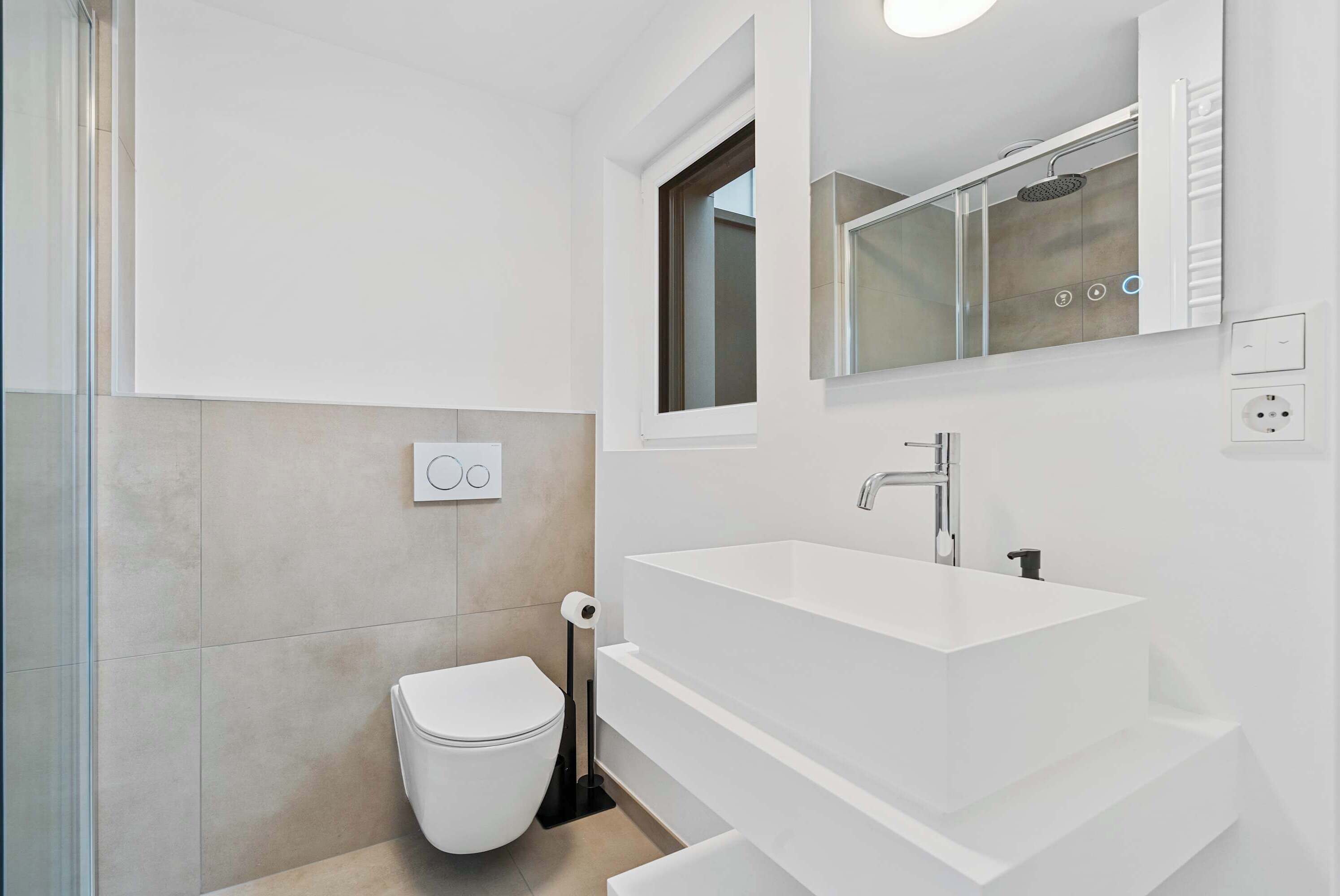 A modern bathroom with a white sink, a toilet, and a glass shower enclosure.
