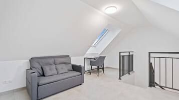 Un dormitorio tipo loft moderno con techo inclinado, un sofá gris, un escritorio pequeño y una silla.