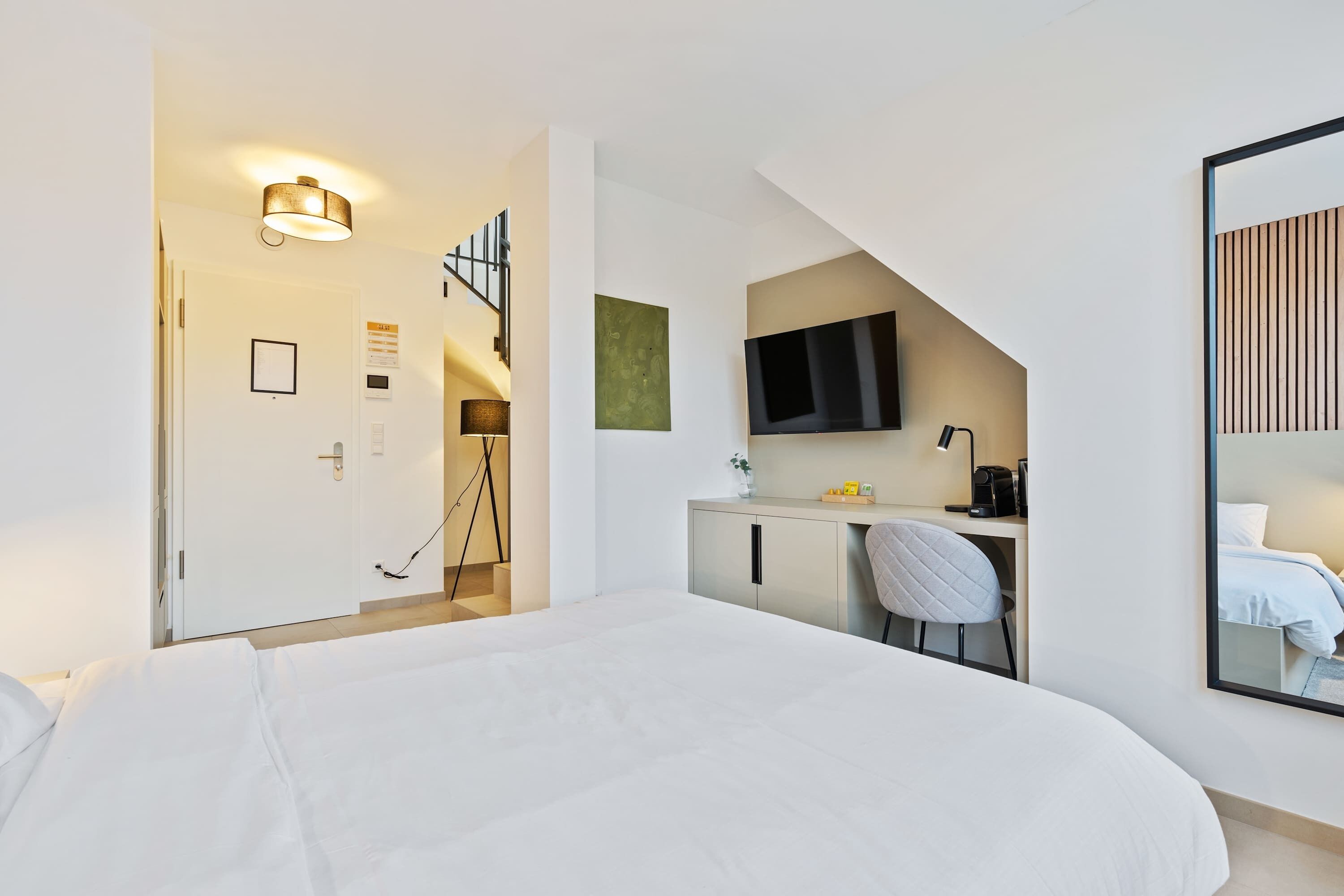 Een hotelkamer met een bed, bureau, stoel en een aan de muur bevestigde televisie.
