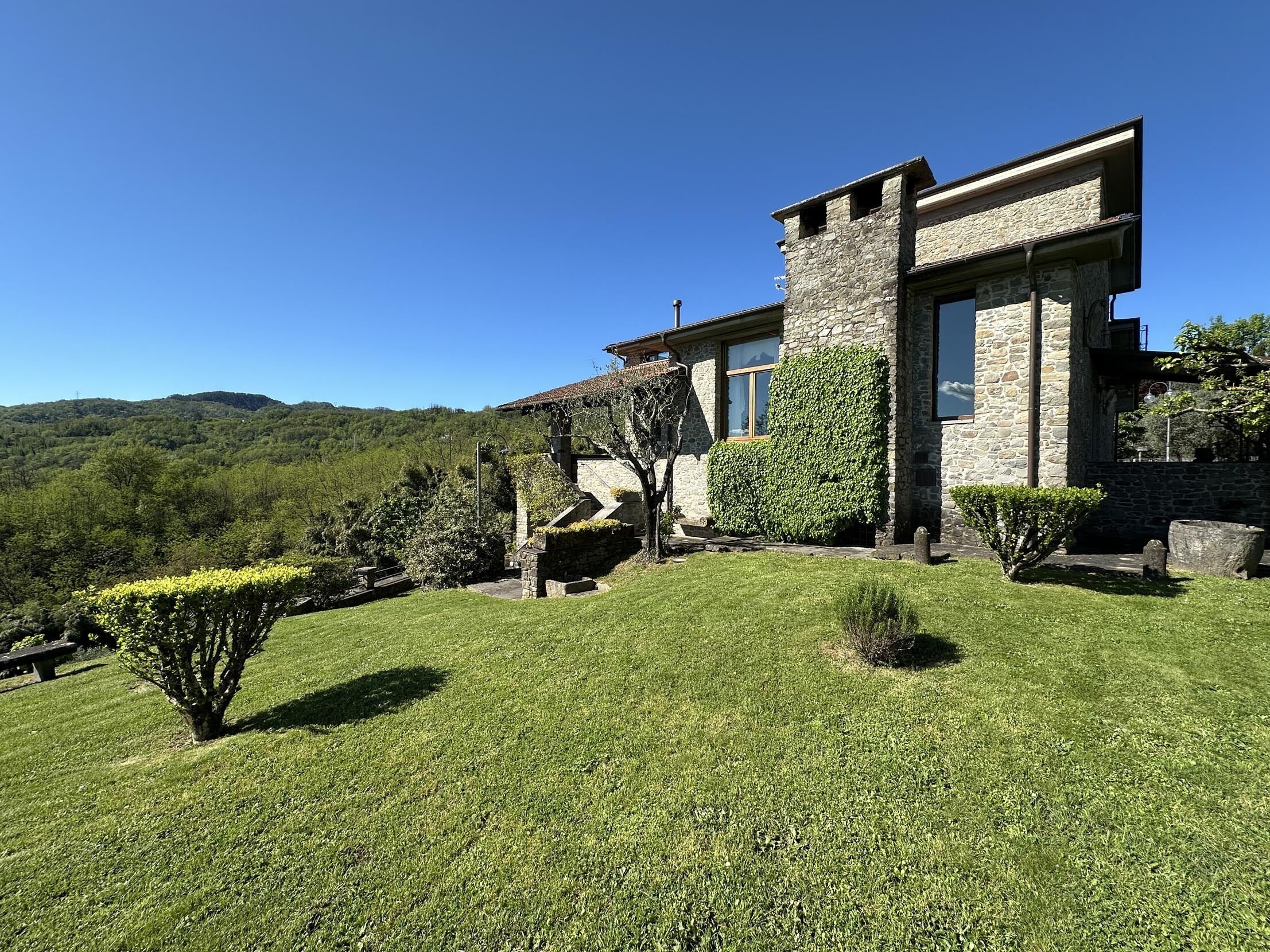 A stone house with a stone staircase leading to the entrance, surrounded by well-maintained grass and small trees.