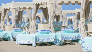 Rows of beach cabanas with canopy tents and lounge chairs, each with a light blue tablecloth and patterned cushions.