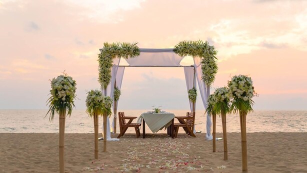 A beach wedding setup with a canopy, floral arrangements, and a table with chairs.