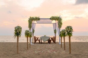 A beach wedding setup with a canopy, floral arrangements, and a table with chairs.