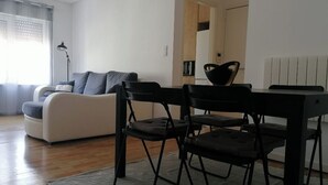 A modern living room with a sofa, a dining table with chairs, and a lamp.