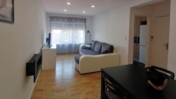 A modern living room with a sofa, a dining table, and a kitchen area in the background.