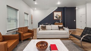 A modern living room with a sofa, armchairs, a coffee table with a bowl and books, and a staircase leading to another level. - Stadium Steps Away | Stylish Townhome w/ Parking (Arlington)