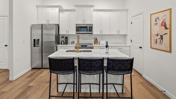 A modern kitchen with white cabinets, stainless steel appliances, and a central island with bar stools. - Stadium Steps Away | Stylish Townhome w/ Parking (Arlington)
