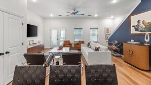 A modern living room with a sofa, two armchairs, a coffee table, and a TV. - Stadium Steps Away | Stylish Townhome w/ Parking (Arlington)