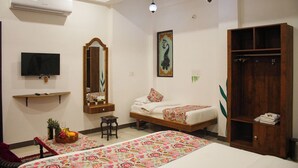 Une chambre d’hôtel avec deux lits, une télévision, un miroir, une armoire et un panier de fruits.