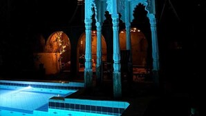 Un espace piscine agrémenté d’une fontaine et d’un kiosque orné de sculptures complexes.
