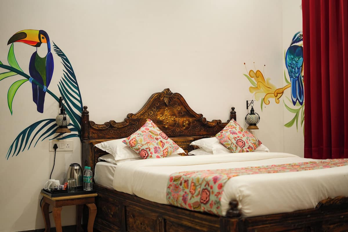 Ein hölzernes Bett mit floraler Bettwäsche, ein Nachttisch mit Wasserkocher und eine Wand mit Vogelmotiven.
