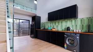 A modern kitchen with a built-in washer, black cabinets, a wooden countertop, and a green tiled backsplash.