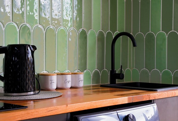 A kitchen counter with a black kettle, two white containers labeled "Tea" and "Coffee," and a black faucet. - 239 High by Regional Escapes (Belmont)