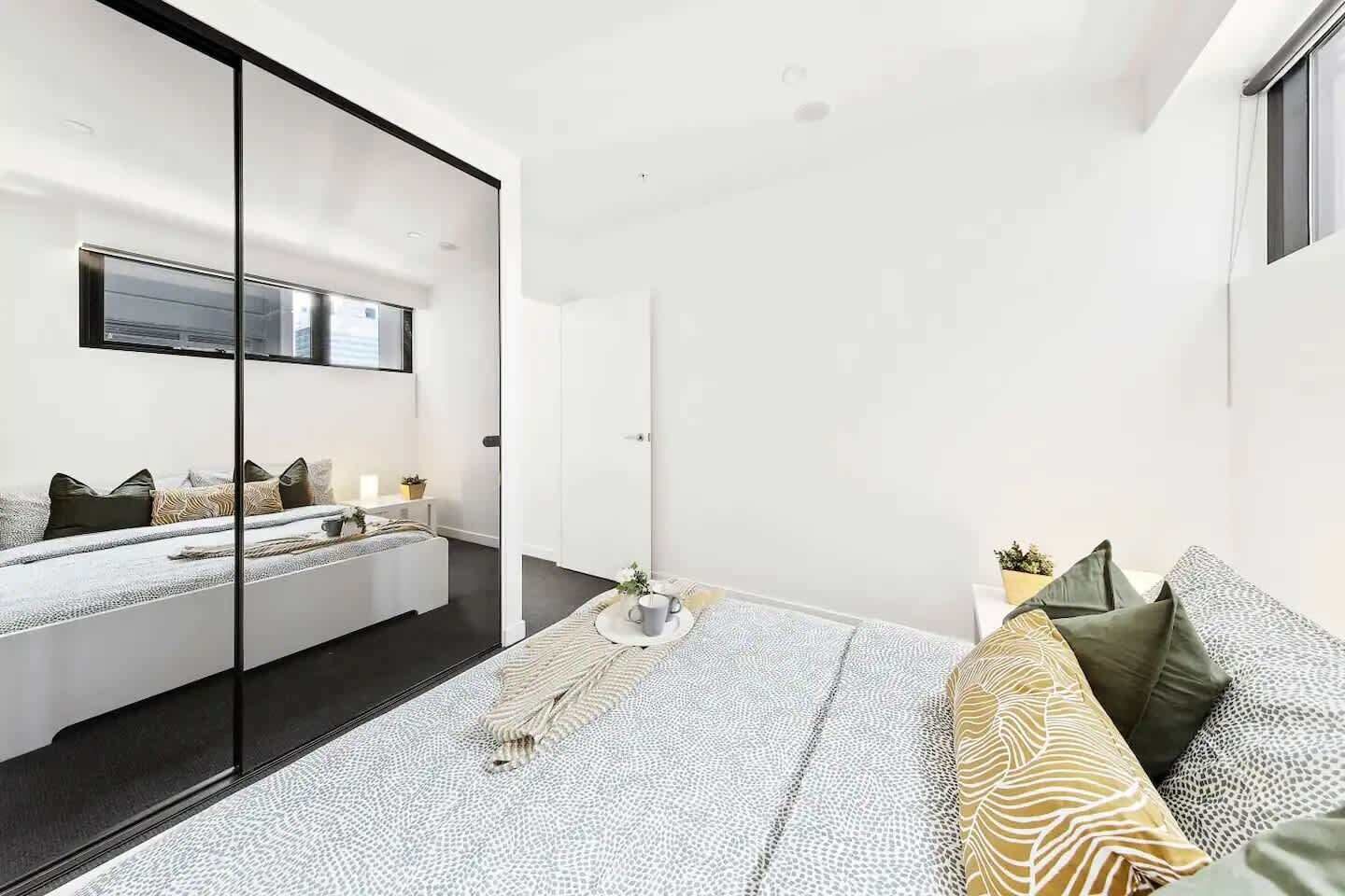 A modern bedroom with a large bed, a sofa, a TV mounted on the wall, and a sliding door leading to another room.