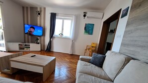 Een woonkamer met een bank, een salontafel, een televisie en een raam met gordijnen.