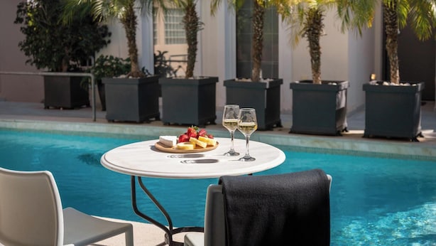 A poolside table with a fruit platter and two glasses of white wine, surrounded by palm trees and a pool. - Serena Calm Pool House (Vari-Voula-Vouliagmeni)